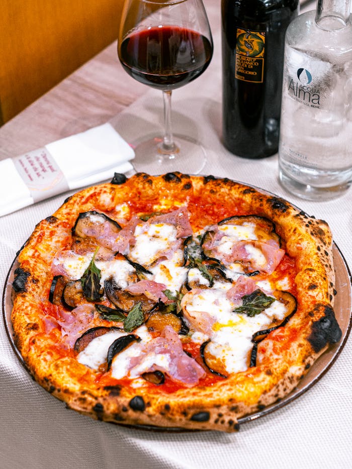 The Art of Drawing Readers In: Your attractive post title goes here Appetizing pizza with mozzarella and ham served with red wine in a cozy restaurant setting.