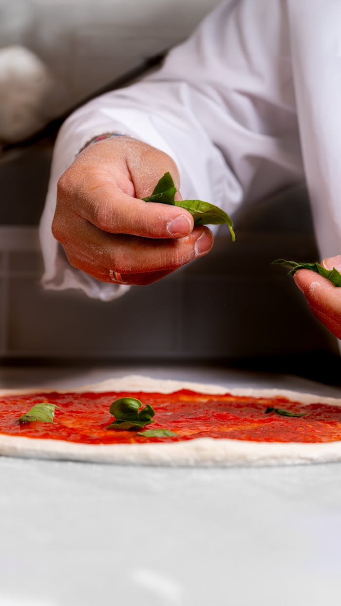 Crafting Captivating Headlines: Your awesome post title goes here Close-up of hands adding basil on pizza dough with tomato sauce.